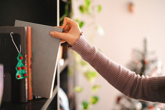 A blonde caucasian female is placing a book on a shelf. The shelf also contains a Christmas tree decoration.