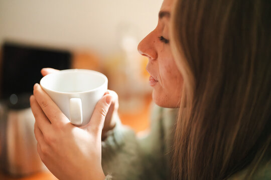 A blonde caucasian woman is drinking from a white mug. She is enjoying a warm beverage, perhaps coffee or tea, in a moment of relaxation.