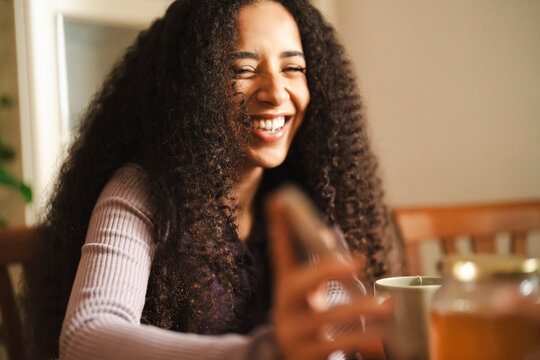 An Arab woman with curly dark hair is laughing at the table. She is enjoying a lighthearted moment, possibly with a blonde Caucasian friend.
