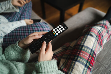 A blonde caucasian female is holding a remote control. She is relaxing on the couch with an Arab female with curly dark hair, watching television.