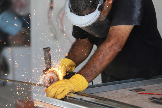 Latino man working on a construction site cutting iron rod with a grinder. Background with copyspace.	
