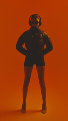 Full-body portrait of stylish young woman combining seasons in one outfit, wearing puffer jacket...