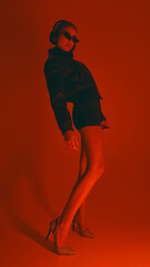 Stylish woman leans back, wearing heels, shorts, puffer jacket and sunglasses, in dynamic pose...