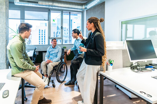 Diverse business team discussing in modern office with disabled colleague in wheelchair