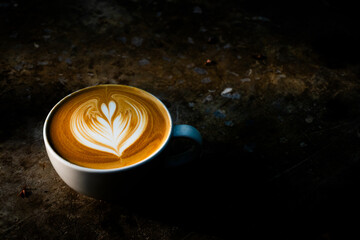 A cup of coffee with latte art pattern in dark mood and tone.	