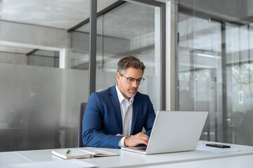 Mature indian ceo business man in suit using pc laptop for trading, looking focused at screen....