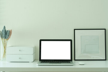 Laptop with a blank screen, coffee cup  and picture frame on white desk, for design mockups or editorial use.