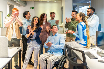 Diverse business team applauding colleague in wheelchair in modern office