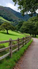 Scenic countryside path alongside wooden fence leading to verdant hills with trees under cloudy sky