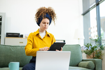 Portrait of a woman using laptop and tablet while sitting on a Green couch at home office