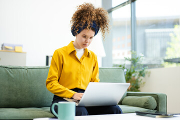 Portrait of a woman using laptop and tablet while sitting on a Green couch at home office