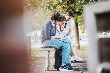 A group of students sitting on a park bench, deeply engaged in studying together, surrounded by greenery. The scene evokes a sense of collaboration and friendship in an outdoor learning environment.