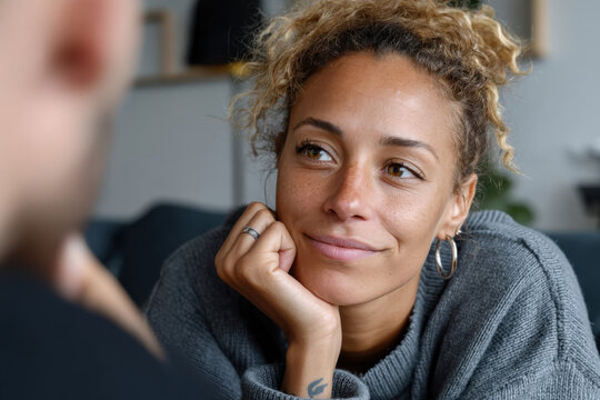 In this heartfelt portrait, a woman with curly hair gazes with a gentle smile, conveying warmth and connection, capturing a moment of genuine interaction between friends.