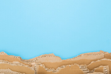 Obraz premium Heap of torn light brown carton on light blue table background. Pastel color. Closeup. Empty place for text. Top down view.