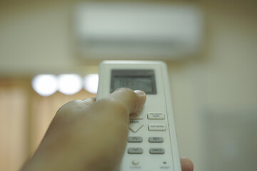 hand using remote controller for adjust Air conditioner inside the room at home