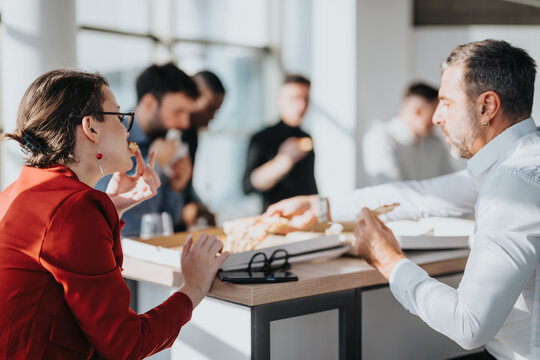 A diverse group of employees collaborating during lunch in a bright, contemporary office space. The setting conveys teamwork, communication, and productivity in a relaxed atmosphere.