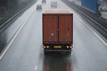 Naklejka premium Truck on highway in heavy rain. Vehicles on the road, with water splashing from tires. Low visibility impacts traffic flow, affecting safety.