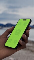 GREEN SCREEN CHROMA KEY person holding a smartphone with a blank green screen on a cloudy morning by the seashore, industrial port and mountains in background