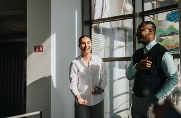 Two multiracial business workers engage in a lively conversation in a modern office. The bright atmosphere highlights collaboration and positive communication.