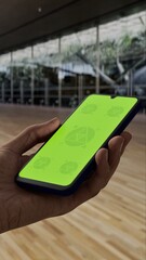 GREEN SCREEN CHROMA KEY Person holding a smartphone with a green screen in a spacious indoor area featuring modern architecture and hardwood flooring