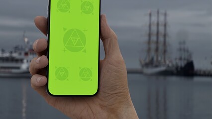 GREEN SCREEN CHROMA KEY Hand holding smartphone with green screen at a harbor on an overcast day,...