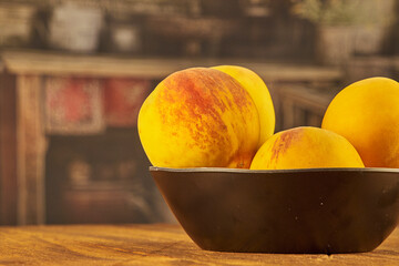 Peaches on a black plate, on a rustic wooden table, in a country kitchen setting.