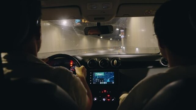 Driving through a tunnel in Morocco at night. Two people are in the car, and the GPS is showing the route. The tunnel is lit up, and the road is wet. POV from the backseat.