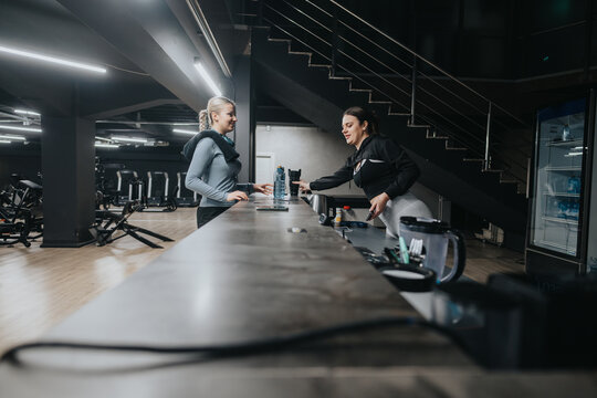A customer and staff member exchange conversation at the reception of a contemporary fitness center, surrounded by gym equipment in a modern environment.