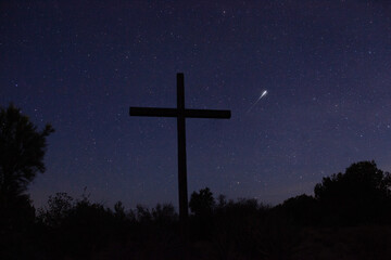 A shooting star beyond a cross on a starry night