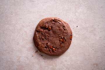 Chocolate cookie with chips on beige stone background. Top view, minimal style, soft natural light. Ideal for packaging, bakery ads, blogs, menus, or social media.