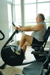 Senior obese man sits on a spin bike to lose weight and exercise in a fitness gym for good health.