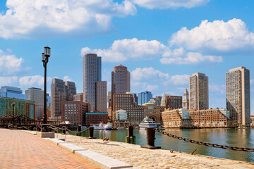 Fototapeta premium Boston's waterfront in daylight, highlighting harbor walk, towering skyscrapers, Rowes Wharf, glistening water, and a vibrant urban setting under a clear blue sky
