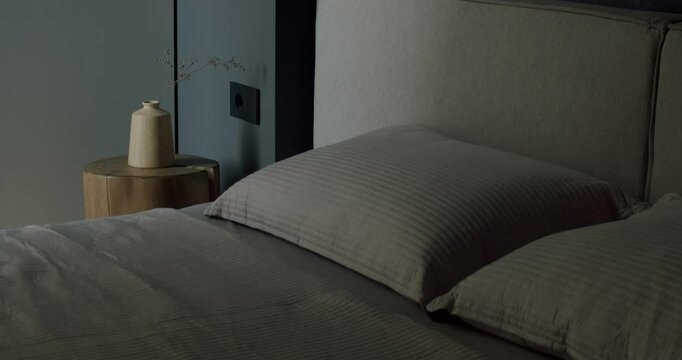 Modern bedroom interior design with neutral colors and minimalist style. Comfortable bed with pillows and soft bedding in a dark, moody atmosphere. Perfect for relaxation.
