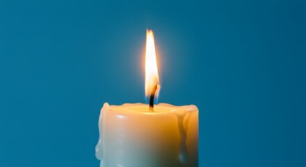 A close up of a burning candle with wax drips against a plain blue color background in studio shot