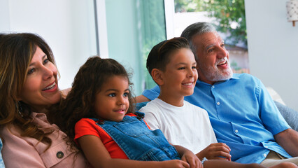 Hispanic Grandparents With Grandchildren Relaxing At Home Sitting On Sofa Watching TV Together