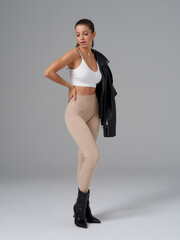 Woman wearing a white crop top, beige leggings, and black ankle boots casually poses with a black...