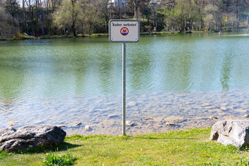 A sign at the lake prohibiting swimming. Clear view of the water and the surrounding nature.