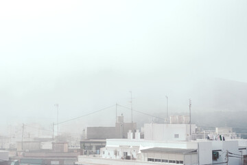 Foggy urban skyline with white rooftops and antennas in soft daylight