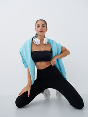Sporty woman kneeling, wearing black tube top and leggings, blue jacket draped over shoulders,...