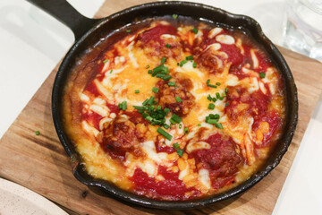 close up of baked meatball in tomato sauce with cheese toppings in a pan on wooden insulating display board