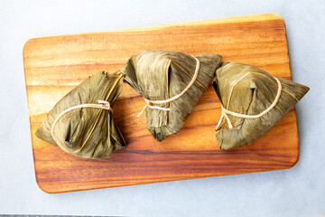 Three Zongzi (also known as Bakcang), savory glutinous rice dumplings wrapped in leaves (likely...