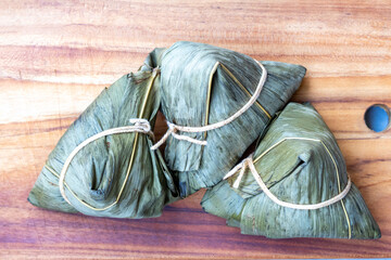 Three Zongzi (also known as Bakcang), savory glutinous rice dumplings wrapped in leaves (likely...