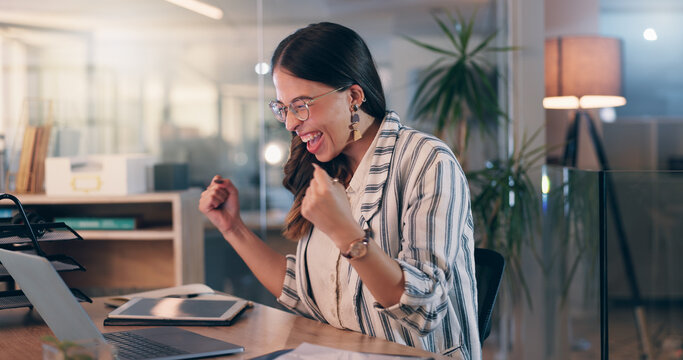 Woman, fist and success with laptop at office, night and celebration for goals, winning or promotion at startup. Person, writer and happy with cheers, bonus or approval for project at creative agency