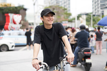handsome young Asian man with hat riding bike on street
