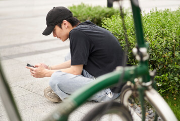handsome young Asian man sitting on ground beside his bike smiling