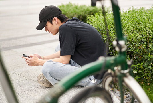 handsome young Asian man sitting on ground beside his bike smiling