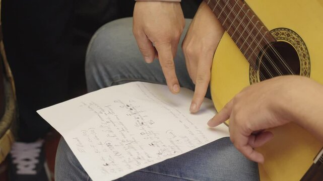 Two pairs of hands point at sheet music during a colombian tiple lesson or practice session. Showing collaboration, learning, and focus on musical skill development.