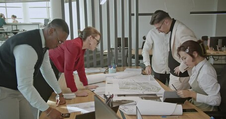 Diverse team of business professionals collaborates on a project, analyzing blueprints and discussing strategies in a modern office.