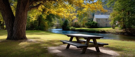 A peaceful riverside scene with a wooden picnic table under a tree, near a flowing stream and a stone cottage in the background.