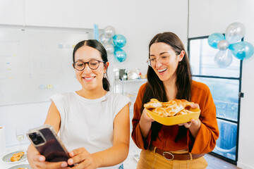 In a festively decorated office, young Latin women take a selfie with traditional food
